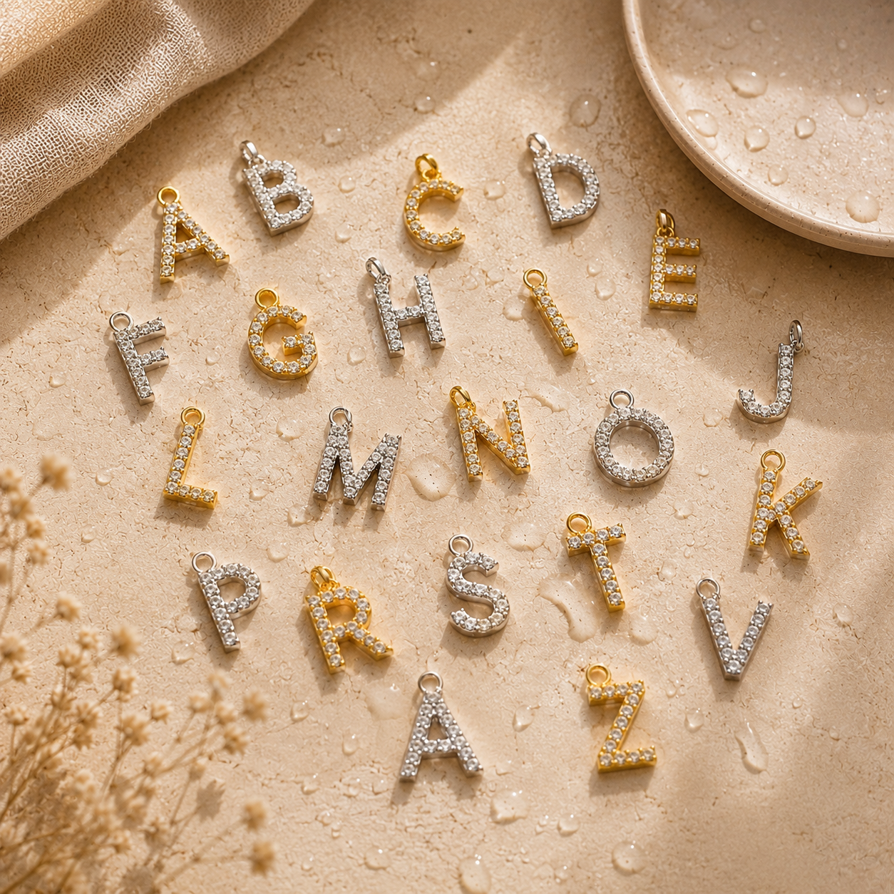Lettres de collier personnalisé en finitions dorée et argentée serties de strass avec gouttes d’eau sur fond crème premium.