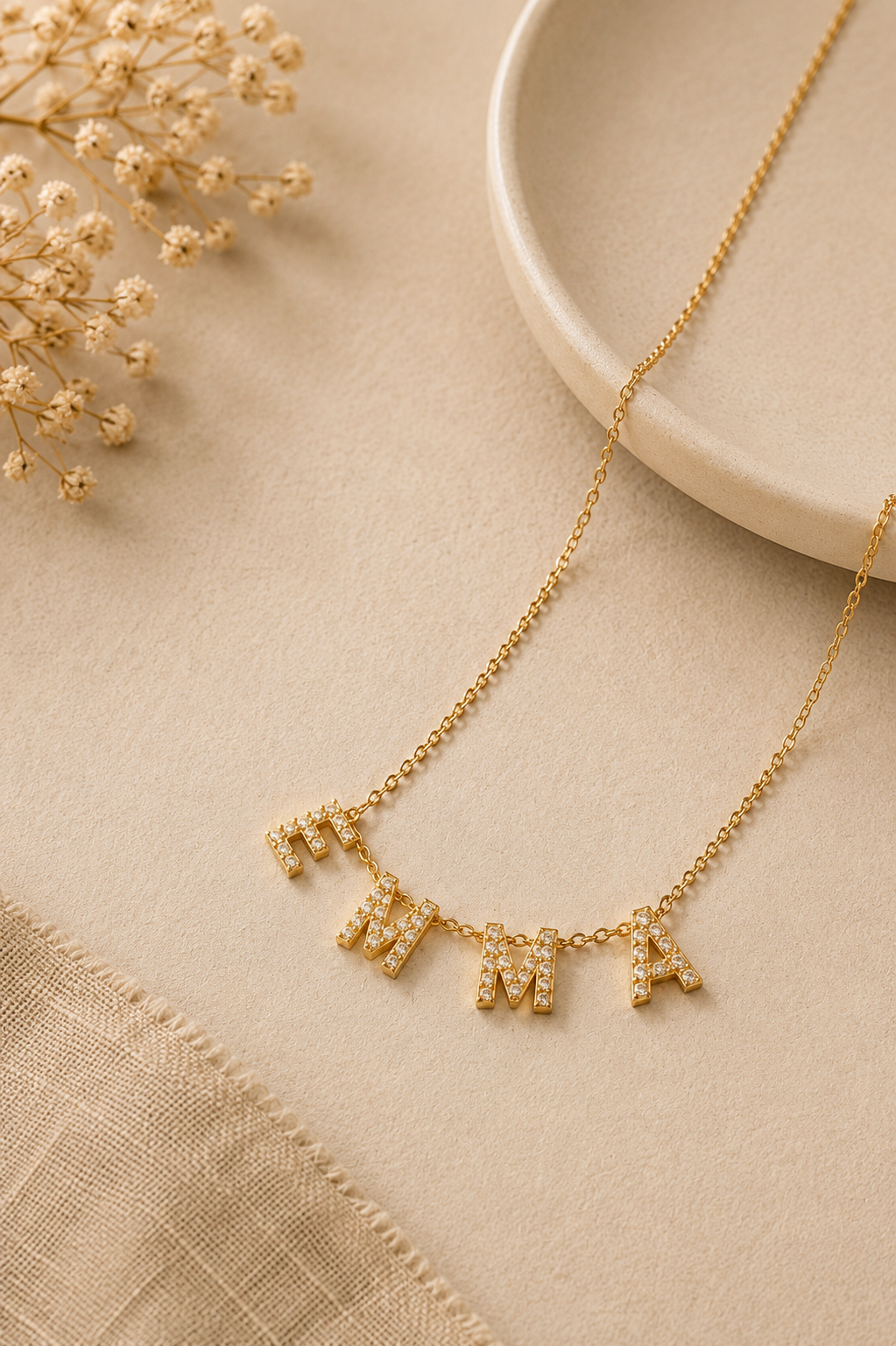 Collier personnalisé prénom EMMA en acier inoxydable doré avec lettres strass sur fond beige minimaliste